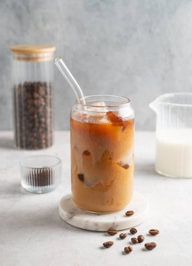 Buzlu latte kahve bardakta, sütlü, mermer bir tahta üzerinde kahve çekirdekleriyle birlikte. Moda yazlık ferahlatıcı içecek konsepti. Ön görünüm, boşluğu kopyala.