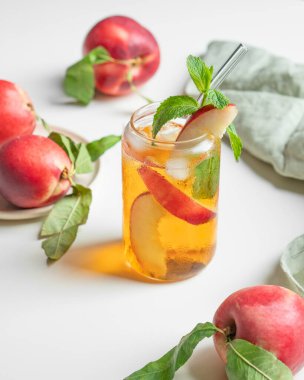 Şeftalili buzlu çay, pencerenin yanındaki beyaz masada bardakta nane şekeri taze meyve, peçete ve güneş ışığı. Bar ya da kafe menüsü için yaz içeceği konsepti. Ön görünüm, boşluğu kopyala.