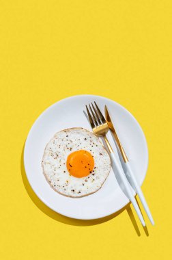 Beyaz tabakta baharatlı ve çatal bıçaklı sahanda yumurta ve gölgeli parlak sarı arka plan. Reklam menüsü ya da afiş kafe için sağlıklı ve hızlı kahvaltı konsepti. Üst görünüm, alanı kopyala.