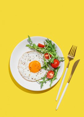Beyaz bir tabakta roka ve kiraz domatesli sahanda yumurta, açık sarı bir zemin ve manevra. Reklam menüsü ya da afiş kafe için sağlıklı kahvaltı konsepti. Üst görünüm, alanı kopyala.
