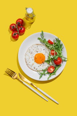 Beyaz bir tabakta roka ve kiraz domatesli sahanda yumurta, açık sarı bir zemin ve manevra ve yağ. Reklam menüsü ya da afiş kafe için sağlıklı kahvaltı konsepti. Üst görünüm, alanı kopyala.