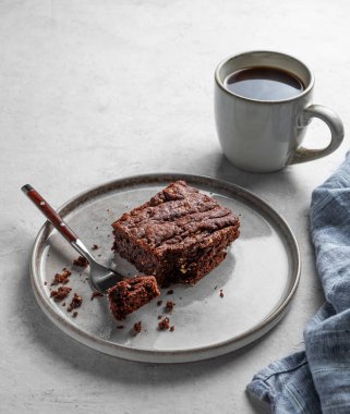 Hafif arka planda bir tabakta çikolatalı kek. Yanında da bir fincan taze kahve ve peçete. Ev yapımı tatlı pişirme konsepti. Ön görünüm, boşluğu kopyala.