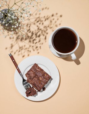 Bej arka planda bir tabakta çikolatalı kek ve bir fincan taze demlenmiş kahve ve bir buket çiçek. Kafe menüsü reklamları ya da afişler için lezzetli hamur işleri kavramı. Üst görünüm, alanı kopyala.