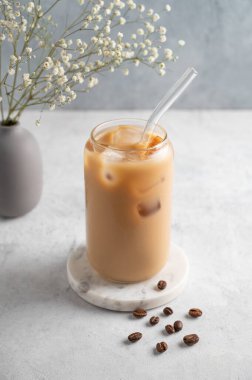 Bir bardak sütlü buzlu latte kahve, arka planda kahve çekirdekleri ve bir buket çigila. Moda yazlık ferahlatıcı içecek konsepti. Boşluğu kopyala.