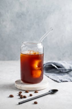 Hafif arka planda buzlu, kahve çekirdeği ve kaşıkla soğuk kahve bardağında. Moda yazlık ferahlatıcı içecek. Ön görünüm, boşluğu kopyala.