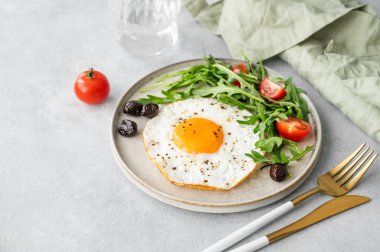 Kavrulmuş yumurta roka, yumurtalar ve hafif arka planda bir tabakta vişne domatesleri bir bardak su, mutfak ve peçeteyle. Kırsal tarzda sağlıklı, hızlı kahvaltı konsepti. Boşluğu kopyala.