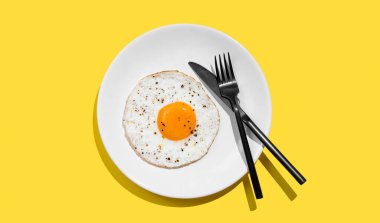 Baharatlı ve siyah çatal bıçaklı sahanda yumurta, beyaz tabakta, parlak sarı arka planda, gölgeli. Reklam menüsü ya da afiş kafe için sağlıklı ve hızlı kahvaltı konsepti. Üst görünüm, alanı kopyala.