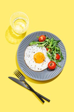 Koyu bir tabakta roka ve kiraz domatesli sahanda yumurta ve bir bardak su. Reklam menüsü ya da afiş kafe için sağlıklı kahvaltı konsepti. Üst görünüm, alanı kopyala.