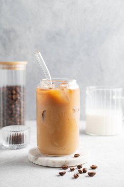 Buzlu latte kahve bardakta, sütlü, mermer bir tahta üzerinde kahve çekirdekleriyle birlikte. Moda yazlık ferahlatıcı içecek konsepti. Ön görünüm, boşluğu kopyala.