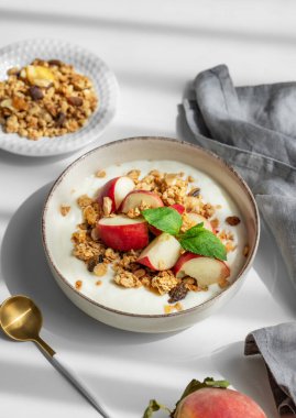 Mısır gevrekli yoğurt ve şeftali, kaşık, peçete ve sabah gölgeleriyle beyaz bir masada. Sağlıklı ve besleyici kahvaltı konsepti. Üst görünüm.