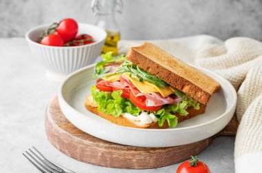 Domuz pastırmalı, peynirli, domatesli, marullu, roka ve soslu tost sandviçi, tahta bir tabakta, arka planda hafif bir peçeteyle. Sağlıklı ve besleyici kahvaltı konsepti. 