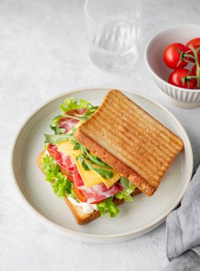 Domuz pastırmalı, peynirli, domatesli, marullu, roka soslu tost ekmeği. Arka planda hafif bir tabakta, bir bardak su ve peçeteyle. Sağlıklı ve besleyici kahvaltı konsepti. Üst görünüm, alanı kopyala.