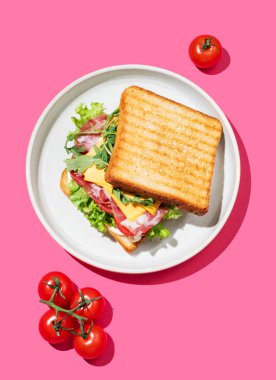 Pastırmalı, peynirli, domatesli, marullu, roka soslu ve parlak pembe arka planda gölgeli tost kulübü sandviçi. Menü reklamcılığı veya sağlıklı yemek afişi için kahvaltı konsepti. Üst görünüm