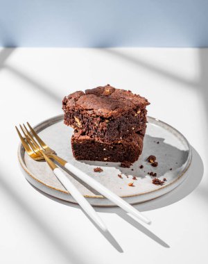 Fındıklı çikolatalı kek, arka planda hafif bir tabakla, çatal bıçak ve gölgelerle dilimlenmiş. Ev yapımı tatlı pişirme konsepti. Ön görünüm, boşluğu kopyala.