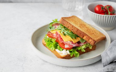 Domuz pastırmalı, peynirli, domatesli, marullu, roka soslu ve hafif arkaplanlı bir tabakta bir bardak suyla. Sağlıklı ve besleyici kahvaltı konsepti. Boşluğu kopyala.