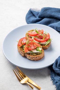 Domatesli sağlıklı susamlı tost, mozzarella, roka ve pesto hafif arka planda mavi bir tabakta, çatal bıçak ve peçeteyle. Kahvaltılık sandviç konsepti. Boşluğu kopyala.