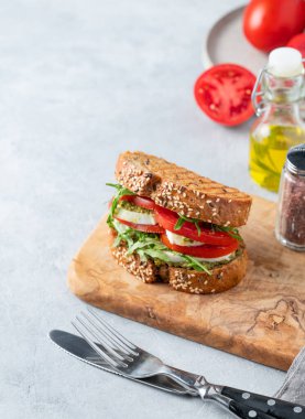 Domatesli tahıllı ekmek, mozzarella, roka ve pesto taze sebzeler, çatal bıçak ve yağlı tahta bir zeminde. Kahvaltılık tost konsepti. Boşluğu kopyala.
