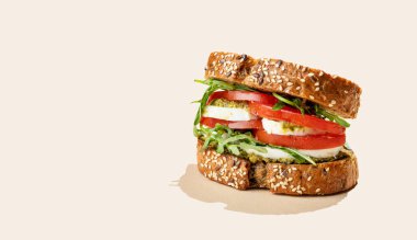 Domatesli tahıllı ekmek, mozzarella roka ve gölgeli parlak bej arka planda pesto. Reklam menüsü ya da afiş için kahvaltılık tost konsepti. Ön görünüm, boşluğu kopyala