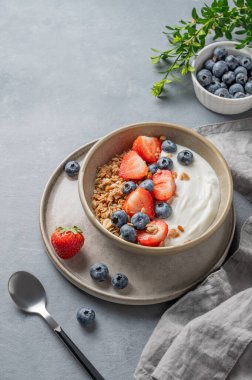 Mısır gevreği, yabanmersini ve çilekli yoğurt mavi arka planda kaşık ve peçeteli bir kasede. Sağlıklı ve besleyici kahvaltı konsepti. Üst görünüm, alanı kopyala.