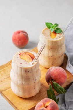 İki bardak şeftalili ve muzlu smoothie, arka planda açık bir tahta üzerinde, tropikal meyveler ve peçeteyle. Sağlıklı beslenme ve detoks diyeti kavramı. Üst görünüm, alanı kopyala.