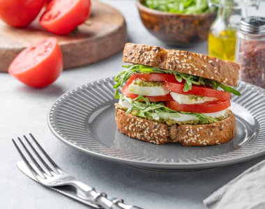 Taze domatesli tahıllı ekmek, mozzarella roka ve pesto hafif bir arka planda, kaplama çatal bıçaklı bir tabak. Sağlıklı beslenme ve beslenme kahvaltısı kavramı. Ön görünüm.