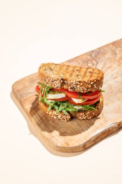 Domatesli tahıllı ekmek, mozzarella roka ve pesto ahşap bir tahtada gölgeli parlak bej bir arka planda. Reklam menüsü ya da afiş için kahvaltılık tost konsepti. Üst görünüm, alanı kopyala