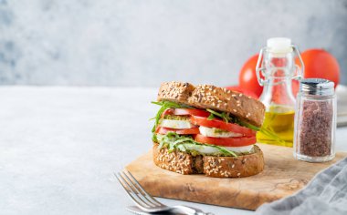 Domatesli tahıllı ekmek, mozzarella, roka ve pesto taze sebzeler, çatal bıçak ve yağ ile arka planda ahşap bir tahta üzerinde. Kahvaltılık tost konsepti. Ön görünüm, boşluğu kopyala.