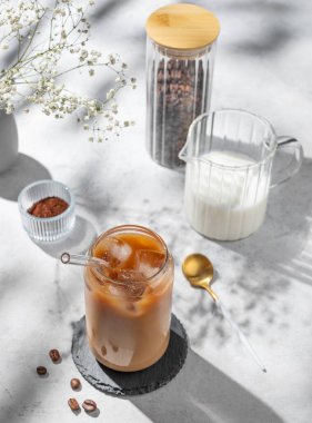 Beyaz arka planda sütlü buzlu latte kahve. Çiçekler, kahve çekirdekleri ve sabah gölgeleri. Moda yazlık ferahlatıcı içecek konsepti. Üst görünüm, alanı kopyala.