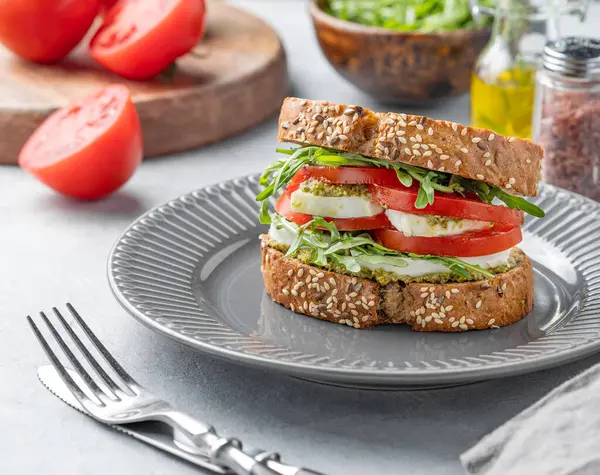 Taze domatesli tahıllı ekmek, mozzarella roka ve pesto hafif bir arka planda, kaplama çatal bıçaklı bir tabak. Sağlıklı beslenme ve beslenme kahvaltısı kavramı. Ön görünüm.