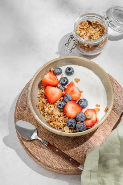 Mısır gevreği, yabanmersini ve çilekli yoğurt. Sabah güneşiyle birlikte arka planda, ahşap bir tahtanın üstünde. Sağlıklı ve besleyici kahvaltı konsepti. Üst görünüm, alanı kopyala.