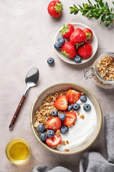 Bal, böğürtlen ve kaşıkla arka planda bir kasede doğal Yunan yoğurdu, yaban mersini ve çilek. Sağlıklı ve besleyici kahvaltı konsepti. Üst görünüm, alanı kopyala.