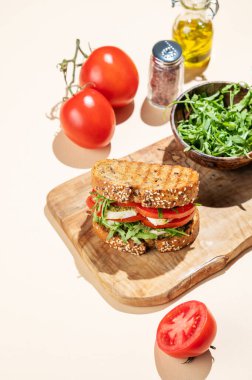 Domatesli tahıllı ekmek ve ahşap bir tahta üzerinde taze sebze ve bitkilerle birlikte mozzarella. Reklam menüsü ya da afiş için kahvaltılık tost konsepti. Üst görünüm, alanı kopyala