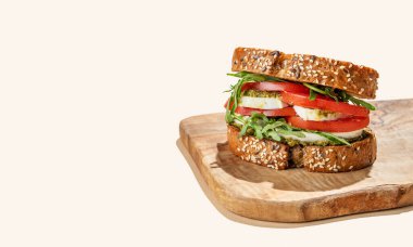 Domatesli tahıllı ekmek, mozzarella roka ve pesto ahşap bir tahtada gölgeli parlak bej bir arka planda. Reklam menüsü ya da afiş için kahvaltılık tost konsepti. Ön görünüm, boşluğu kopyala