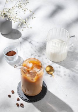 Beyaz arka planda sütlü buzlu latte kahve. Çiçekler, kahve çekirdekleri ve sabah gölgeleri. Moda yazlık ferahlatıcı içecek konsepti. Üst görünüm, alanı kopyala.