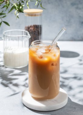 Bir bardak sütlü buzlu latte kahve, açık arka planda mermer bir tezgah, dallı ve sabah gölgeli. Moda yazlık ferahlatıcı içecek konsepti. 