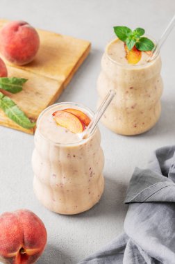 İki bardak şeftalili ve muzlu smoothie. Arka planda, tropikal meyve ve peçeteli. Sağlıklı beslenme ve detoks diyeti kavramı. Üst görünüm, alanı kopyala.