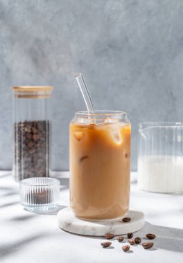 Kahve çekirdekleri ve sabah gölgeleriyle mermer tezgahta sütlü buzlu latte kahve. Moda yazlık ferahlatıcı içecek konsepti. Ön görünüm, boşluğu kopyala.