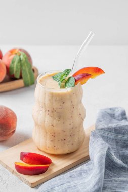 Şeftalili meyve püresi ve muzlu meyve suyu, bir bardak içinde tahta bir tahta üzerinde, arka planda, tropikal meyve dilimleriyle. Sağlıklı beslenme ve detoks diyeti kavramı. Ön görünüm, boşluğu kopyala.