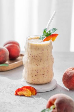 Şeftalili ve muzlu meyve püresi, cam kenarında açık bir arka planda, tropikal meyveler ve sabah güneşiyle birlikte. Sağlıklı beslenme ve detoks diyeti kavramı. Ön görünüm, boşluğu kopyala.