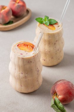 İki bardak şeftalili ve muzlu smoothie. Hafif bir arka planda, tropikal meyveli. Reklam menüsü kafesi veya afişi için sağlıklı beslenme ve detoks diyeti kavramı. 