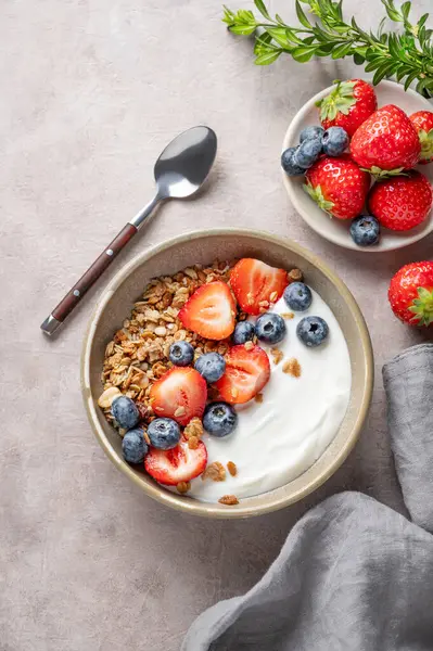Arka planda böğürtlenli, peçeteli ve kaşıklı yaban mersini ve çilekli doğal Yunan yoğurdu. Sağlıklı ve besleyici kahvaltı konsepti. Üst görünüm, alanı kopyala.