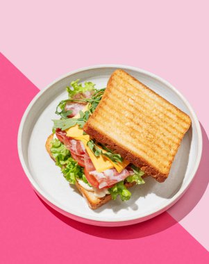 Pastırmalı, peynirli, domatesli, marullu, roka soslu ve pembe arkaplanlı bir tost ekmeği. Menü kafenin reklam afişi için sağlıklı ve besleyici kahvaltı konsepti. Üst görünüm.