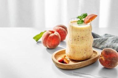 Şeftalili meyve suyu ve muzlu meyve suyu. Bardakta, tahta bir tahta üzerinde. Pencerenin yanındaki beyaz masada. Sağlıklı beslenme ve pankart kafenin reklam merusu için detoks diyeti kavramı. Ön görünüm, boşluğu kopyala.