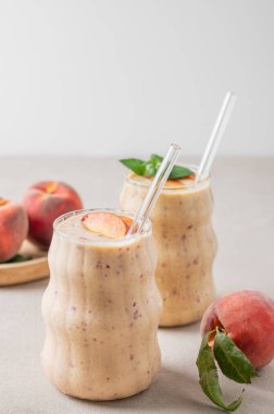 İki bardak şeftalili ve muzlu smoothie. Hafif bir arka planda, tropikal meyveli. Sağlıklı beslenme ve reklam menüsü kafesi ya da afişi için detoks diyeti kavramı. Ön görünüm, boşluğu kopyala.