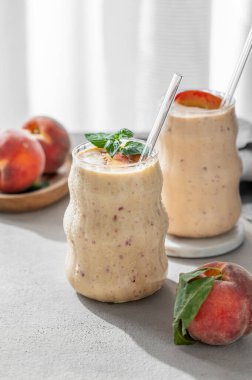 İki bardak şeftalili ve muzlu smoothie. Pencerenin yanındaki beyaz masada, tropik meyve ve sabah güneşiyle birlikte. Sağlıklı beslenme ve pankart kafenin reklam merusu için detoks diyeti kavramı. Ön görünüm, boşluğu kopyala.