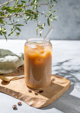 Sütlü buzlu sütlü sütlü sütlü sütlü latte kahve, arka planda hafif dallı ve sabah gölgeli. Moda yazlık ferahlatıcı içecek konsepti.
