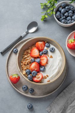 Mısır gevreği, yabanmersini ve çilekli yoğurt mavi arka planda kaşık ve peçeteli bir kasede. Sağlıklı ve besleyici kahvaltı konsepti. Üst görünüm, alanı kopyala.