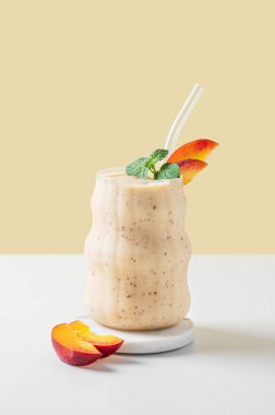 Şeftalili, muzlu ve nane arkaplanda sarı beyaz bir fonda tropikal meyveli bir bardakta. Reklam menüsü ya da afiş kafe için sağlıklı beslenme ve detoks diyeti kavramı. Ön görünüm, boşluğu kopyala.