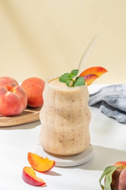 Şeftalili ve muzlu meyve suyu mermer tezgahın üzerinde tropikal meyveler, güneş ışığı ve peçeteli sarı beyaz bir arka planda. Reklam menüsü ya da afiş kafe için sağlıklı beslenme ve detoks diyeti kavramı. Ön görünüm, boşluğu kopyala.