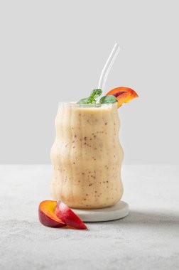 Şeftalili ve muzlu meyve püresi mermer tezgahın üzerinde tropikal meyve dilimleri ve güneş ışığıyla aydınlık bir zeminde. Reklam menüsü ya da afiş kafe için sağlıklı beslenme ve detoks diyeti kavramı. Ön görünüm, boşluğu kopyala.